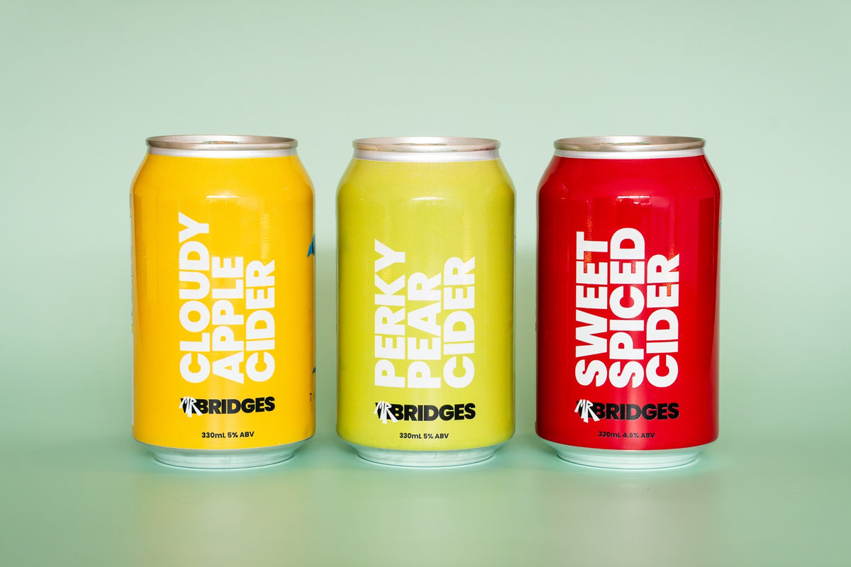 The cans of Mr Bridges cider, Cloudy Apple Cider (yellow), Perky Pear Cider (reen), Sweet Spiced Cider (red)