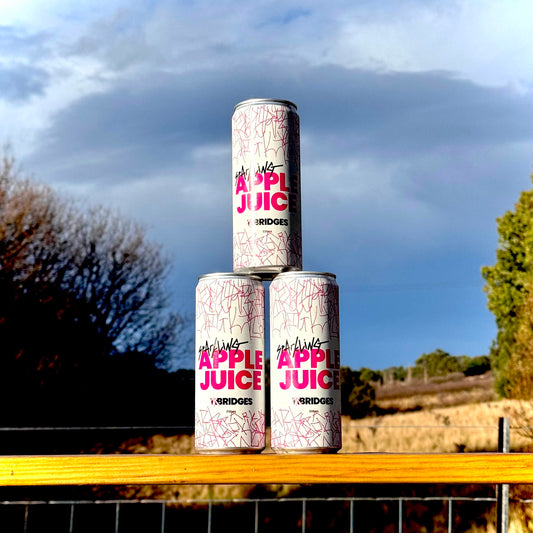 Three cans of Mr Bridges Sparkling Apple Juice stacked on a fence rail at Trial Bay Orchards, Tasmania