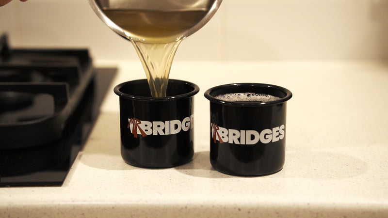 Two black mr bridges cups with sweet spiced cider being poured into them.